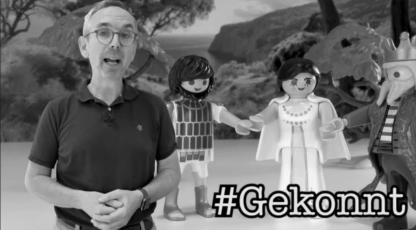 Mann vor Playmobil-Figuren, spricht; Schriftzug '#Gekonnt' im Vordergrund.